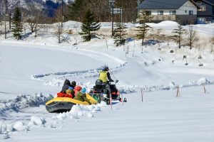 People enjoying snow rafting pulled by snowmobile during winter in Hokkaido, Japan.