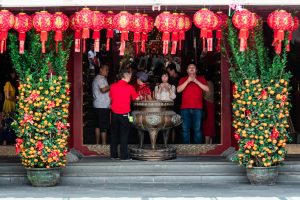 People praying at a Chinese temple in Singapore, adorned with lanterns and decorations for an auspicious celebration.