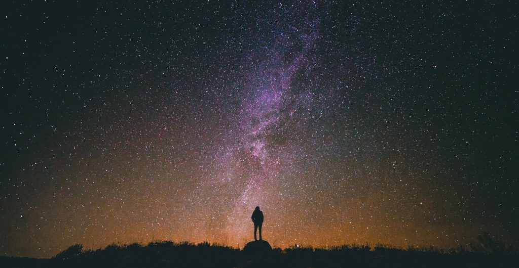 Person silhouetted against a breathtaking night sky filled with stars and the Milky Way galaxy.