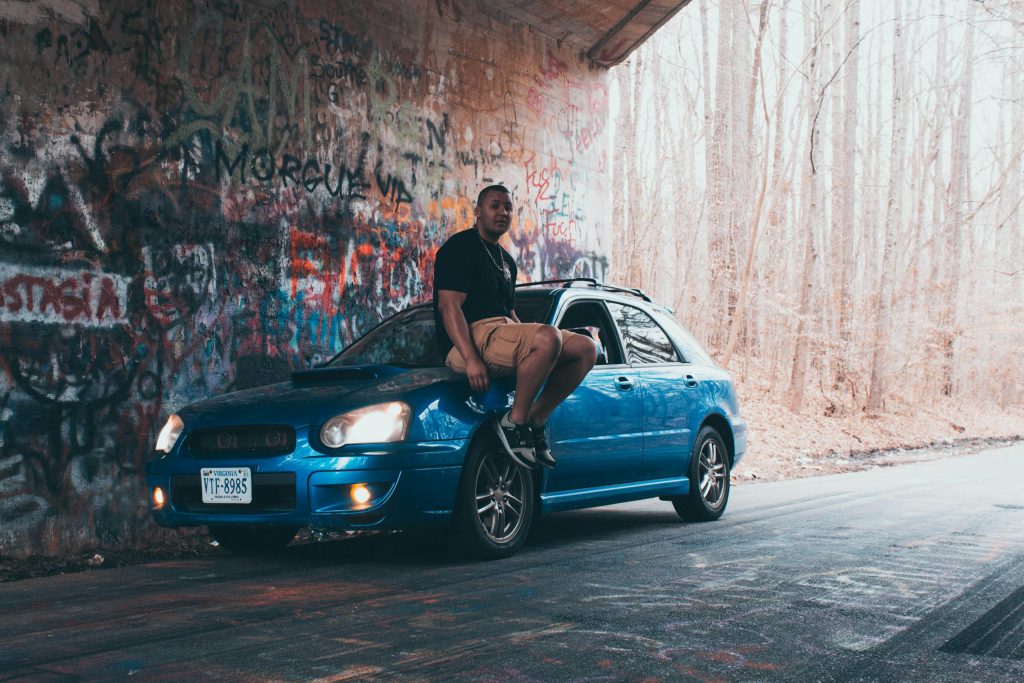 Person sitting on a blue car under a graffiti-covered bridge in Williamsburg, VA.