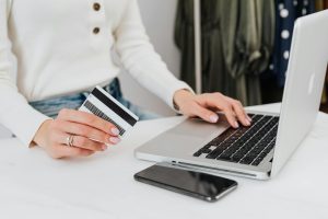 Person using laptop for online shopping, holding a credit card, closeup.