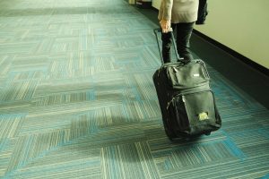 Person walking with luggage on blue carpeted airport corridor, traveling