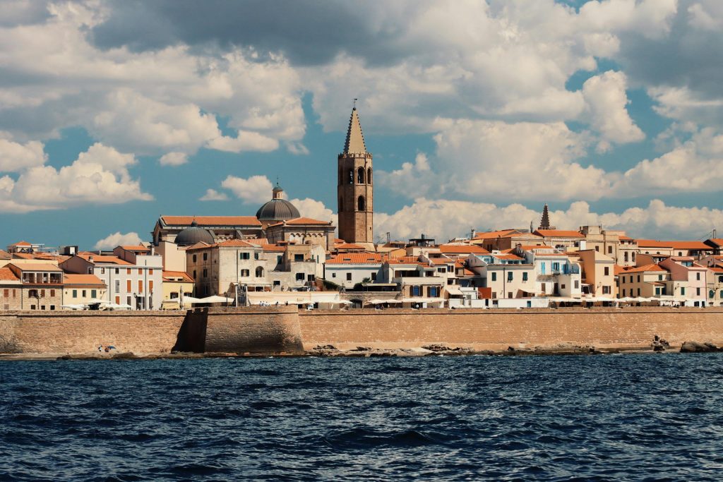 Picturesque view of Alghero's waterfront with historic architecture and vibrant skyline under a clear sky.