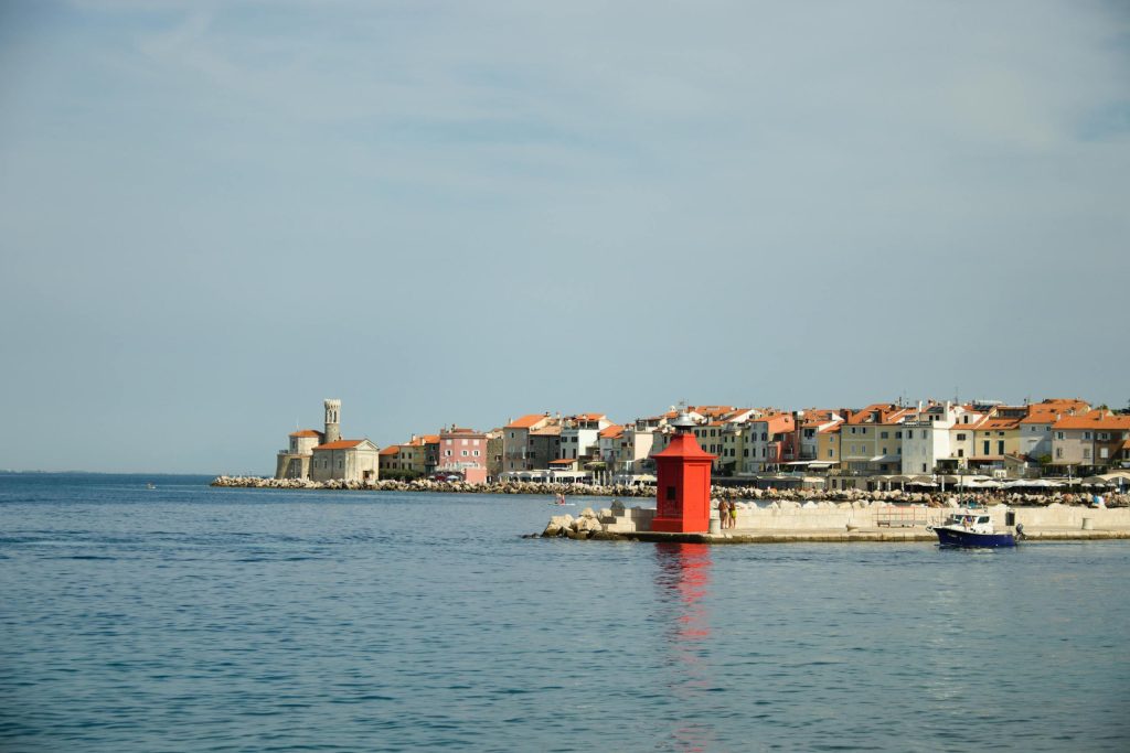 Picturesque view of Piran harbor in Slovenia with colorful buildings and a vibrant red lighthouse.
