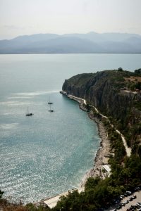 Scenic aerial view of Nafplion's rocky coastline with sailboats drifting in the glistening sea.