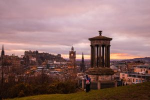 Scenic view of Edinburgh city skyline at sunset from Calton Hill, featuring historic architecture.