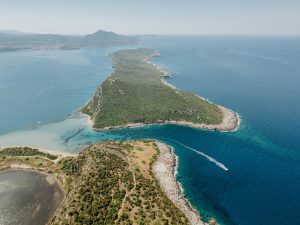 Stunning aerial view of a lush green peninsula surrounded by clear blue waters, perfect for travel inspiration.