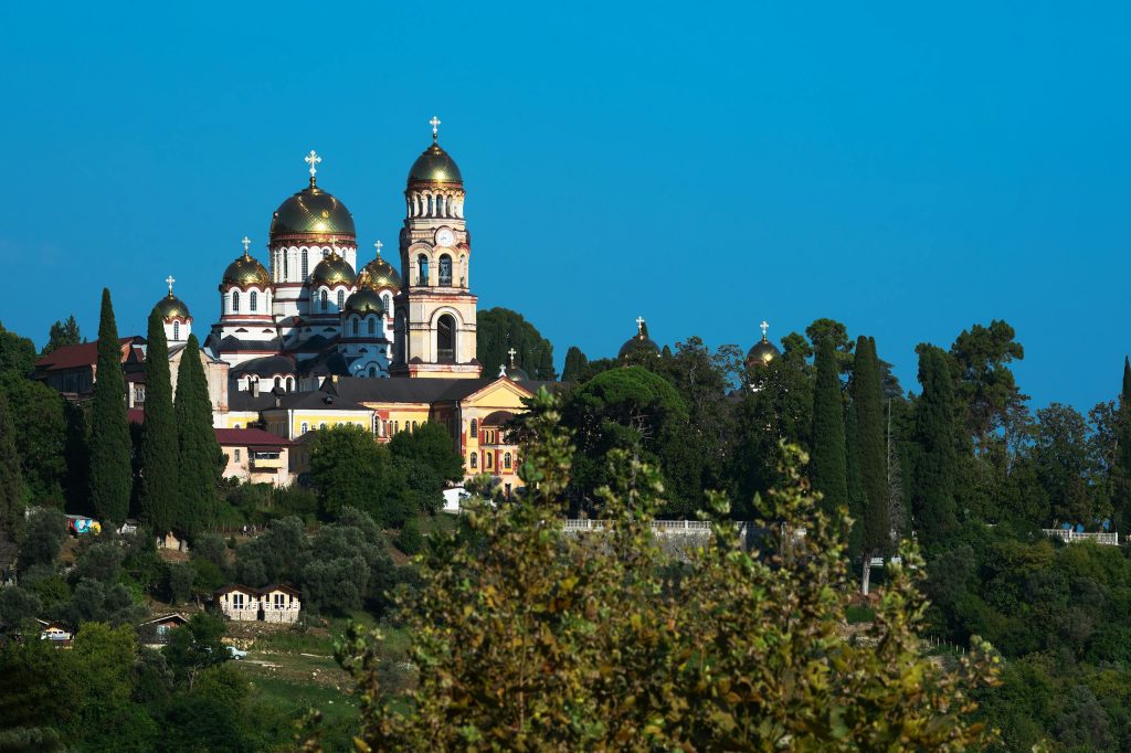 Stunning landscape of New Athos Monastery surrounded by greenery under a clear blue sky.