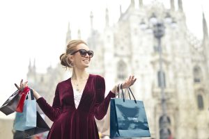 Stylish woman in sunglasses enjoys shopping in front of Milan Cathedral, holding shopping bags.