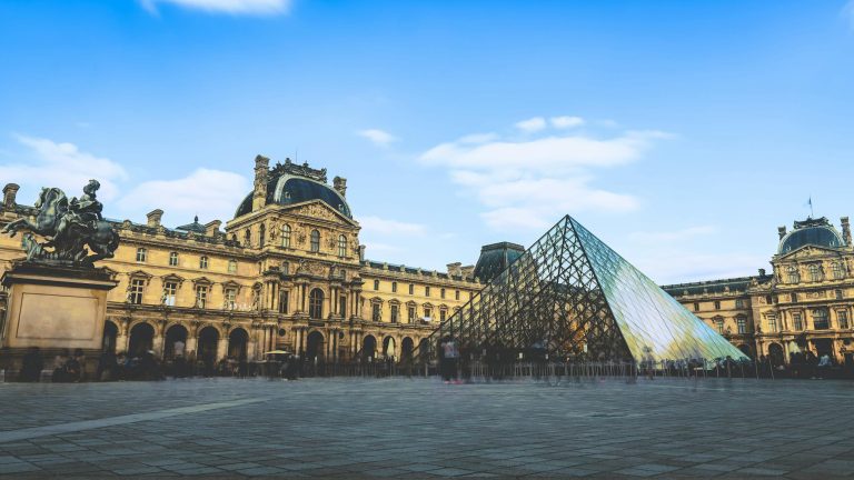 The iconic glass pyramid of the Louvre Museum against a clear blue sky in Paris.