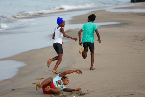 Three children playing and running joyfully on the sandy beach in Charlestown, Saint Kitts and Nevis.