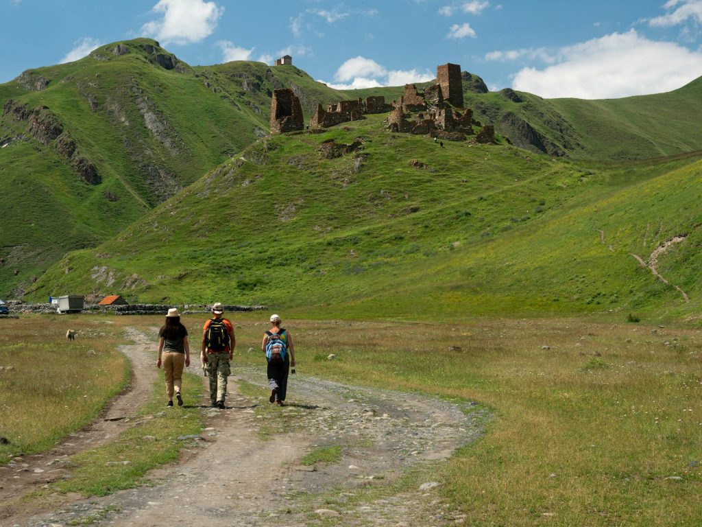 Three hikers walk towards ancient ruins in the scenic mountains of Mtskheta-Mtianeti, Georgia.