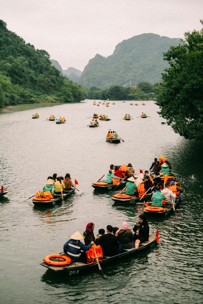 Tourists enjoy a serene rowboat ride on a lush river surrounded by mountains.