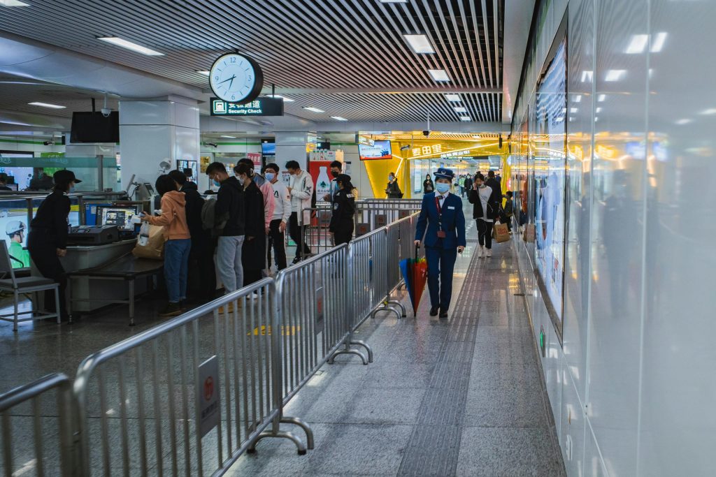 Travelers passing through airport security with staff and metal railings visible.