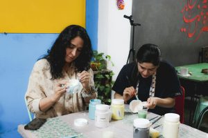 Two women engaged in painting ceramics at a creative workshop indoors.