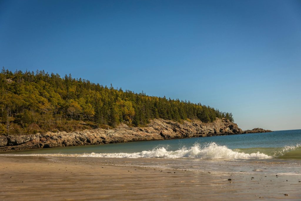 Waves crashing on a sandy beach with rugged cliffs in Acadia National Park.