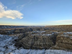 Wide view of the rugged Badlands landscape with snow patches under a clear blue sky.