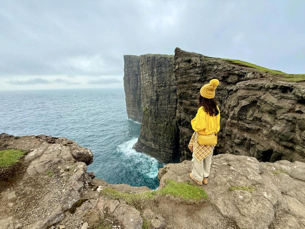 Woman in yellow clothing on cliff edge overlooking scenic ocean view.