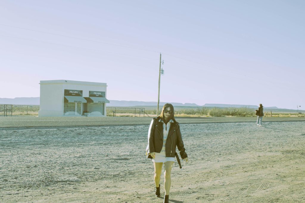 Woman walking near the iconic Prada Marfa installation in Valentine, Texas desert.
