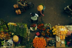 A bustling street market scene with people and colorful flowers viewed from above.