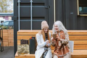 A grandmother and granddaughter share a happy moment with shopping bags outdoors.