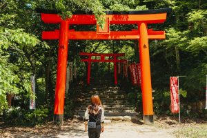 A woman approaches the vibrant red torii gates of Tenkai Inari Shrine in Fukuoka, Japan, surrounded by lush greenery.