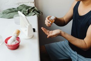 Adult man applying aftershave in a casual bathroom setup with mirror and shaving accessories.