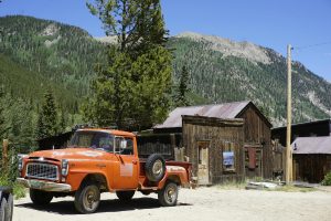Classic orange pickup truck parked in front of rustic wooden houses in Saint Elmo, Colorado.