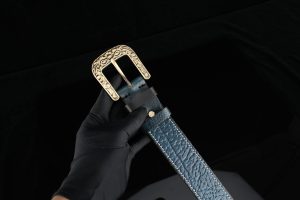 Close-up of a blue leather belt with an ornate gold buckle, held in a gloved hand.