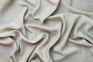 Close-up of luxurious silver satin fabric showcasing rippled texture and smooth folds.
