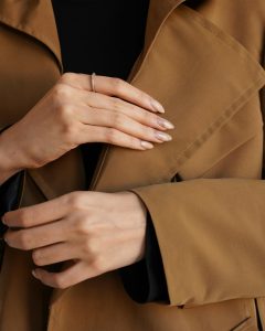 Close-up of woman's hands in a brown coat showcasing minimalist silver ring.