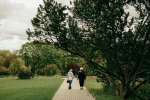 Elderly women strolling down a paved path in a lush Belarusian park on a cloudy day.