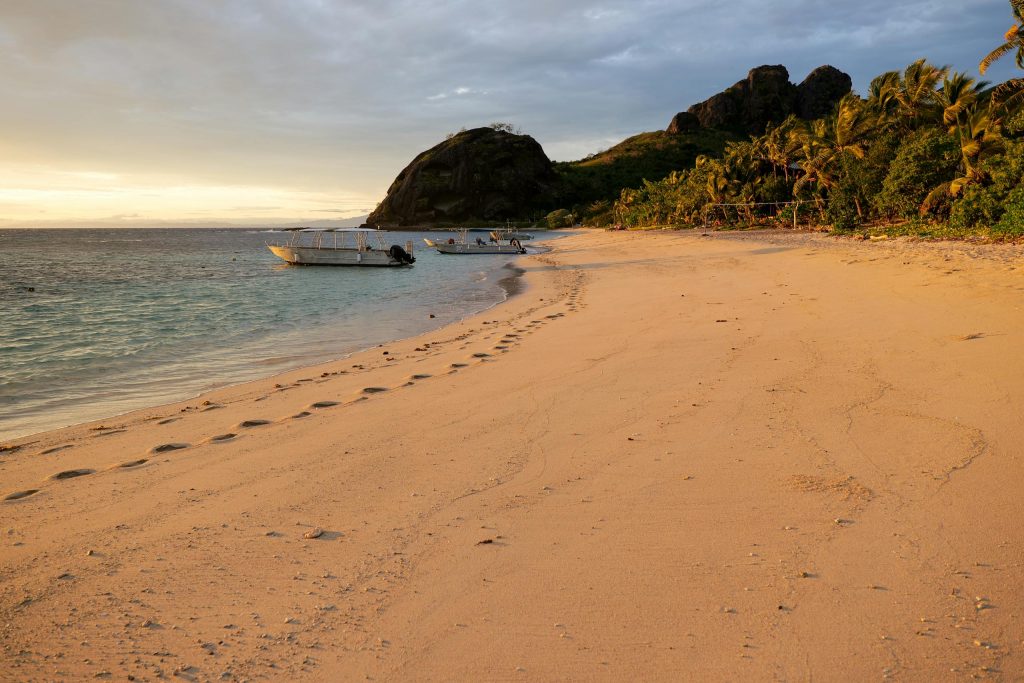 Tranquil evening beach scene with boats and palm trees on Yasawa Islands, Fiji.